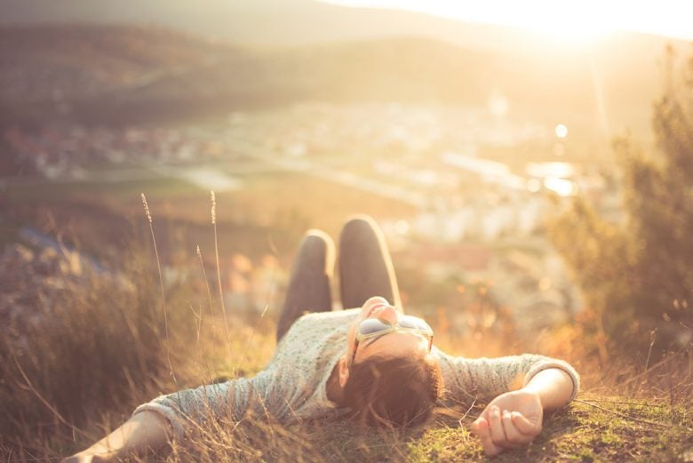 smiling person lying on a grassy hill on a sunny day