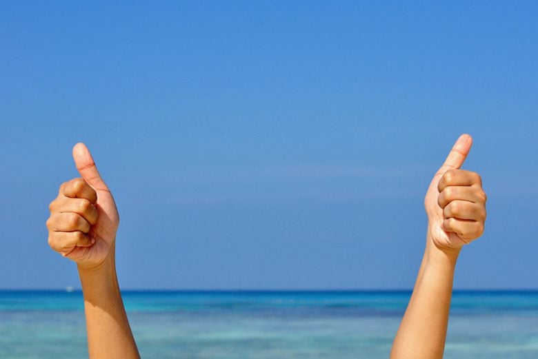 Person giving two thumbs up by the ocean