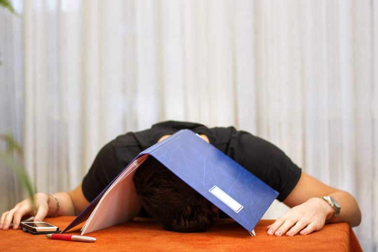 a man lying on a desk with a folder over his head
