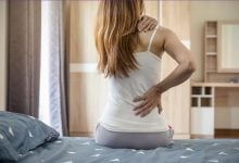 Woman sitting up in bed with neck and back pain