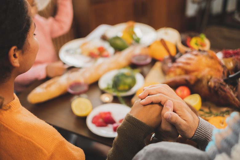 Family gathered around table, holding hands, saying blessing