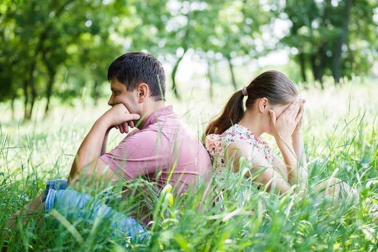 Man and woman sitting back to back in field of grass