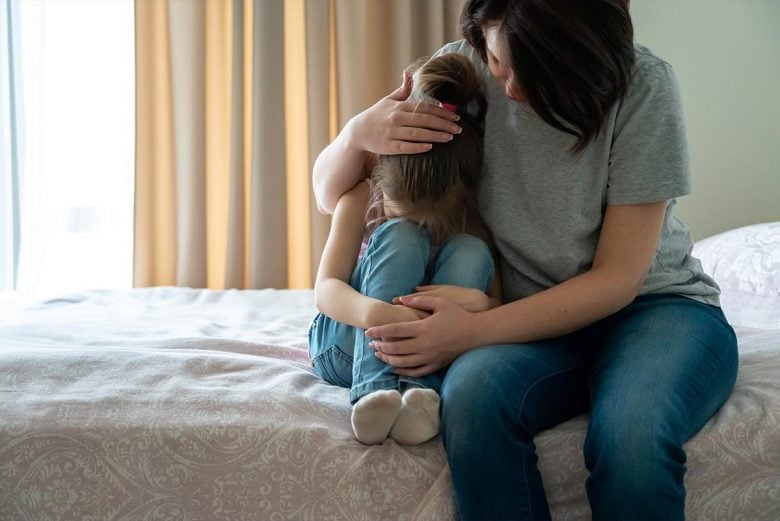 Mother comforting child on bed - how to protect your child from negative energy