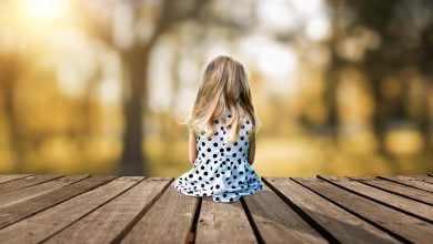 A little young girl is sitting on a wooden pier