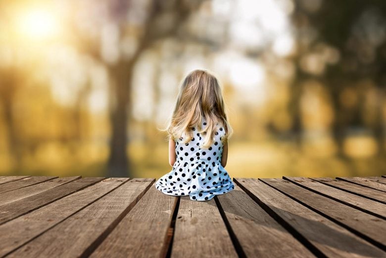 A little young girl is sitting on a wooden pier