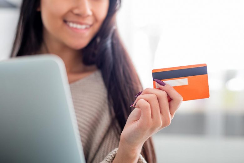 Woman smiling at laptop holding credit card