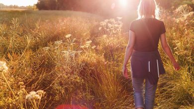 Woman walking away in field at sunset