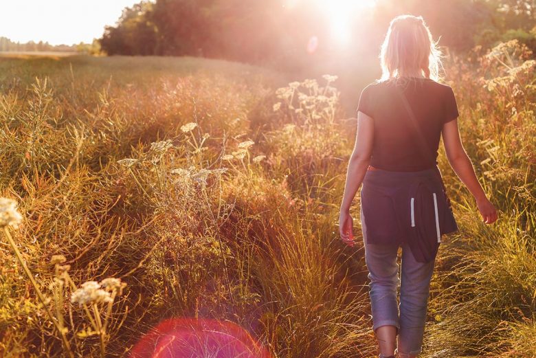 Woman walking away in field at sunset