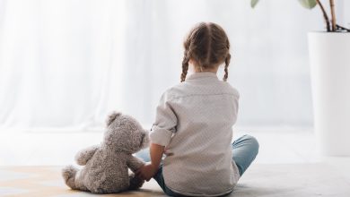 rear view of little child sitting on floor with her teddy bear toy