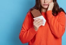 Woman eating chocolate bar looking sad