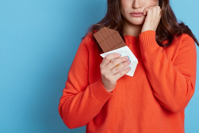 Woman eating chocolate bar looking sad